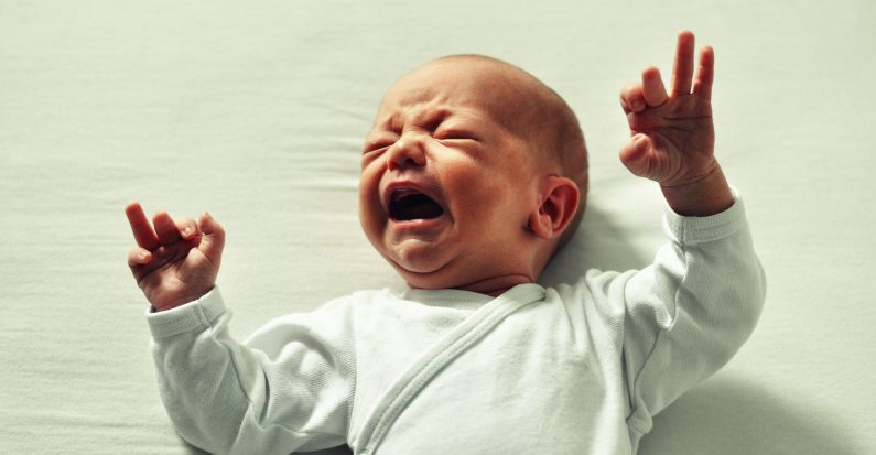 Un bébé sur un lit blanc qui pleure