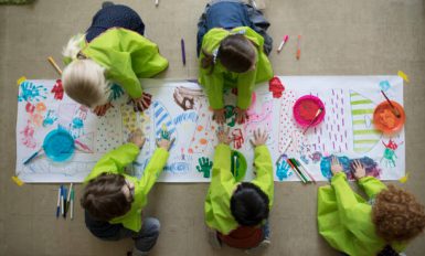 5 enfant qui dessinent sur une grande feuille blanche