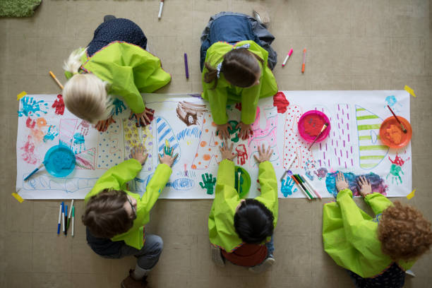 5 enfant qui dessinent sur une grande feuille blanche